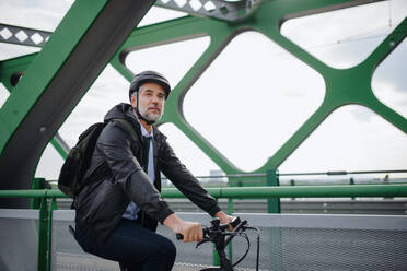 Ein Geschäftsmann auf dem Weg zur Arbeit, der mit dem Fahrrad über eine Brücke fährt, ein Konzept für nachhaltigen Lebensstil. - HPIF01773