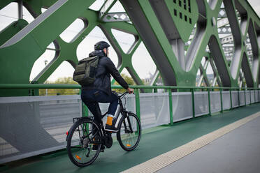 Rückansicht eines Geschäftsmannes auf dem Weg zur Arbeit, der mit dem Fahrrad über eine Brücke fährt, Konzept des nachhaltigen Lebensstils. - HPIF01774