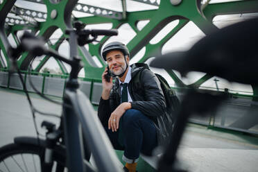 A businessman with bike sitting on bench, using smartphone. Commuting and alternative transport concept - HPIF01775