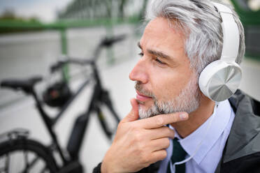 A businessman with bike sitting on bench, listening to music and resting. Commuting and alternative transport concept - HPIF01782