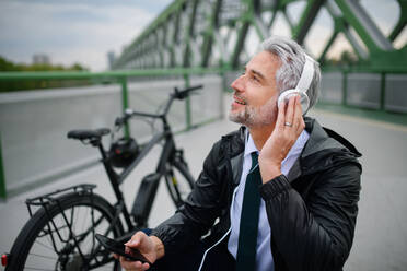 Ein Geschäftsmann mit Fahrrad sitzt auf einer Bank, hört Musik und ruht sich aus. Pendeln und alternatives Verkehrskonzept - HPIF01783