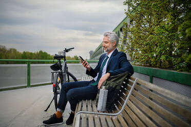 Ein Geschäftsmann mit Fahrrad auf einer Bank sitzend, Musik hörend, die Füße hochgelegt und sich ausruhend. Pendeln und alternatives Verkehrskonzept - HPIF01786