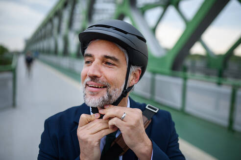 Porträt eines Geschäftsmannes, der auf dem Weg zur Arbeit einen Fahrradhelm aufsetzt, Konzept des nachhaltigen Lebensstils. - HPIF01790