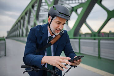 Ein Geschäftsmann auf dem Weg zur Arbeit, der sein Fahrrad auf der Brücke schiebt und eine SMS auf seinem Handy schreibt, ein nachhaltiges Lebensstilkonzept. - HPIF01791