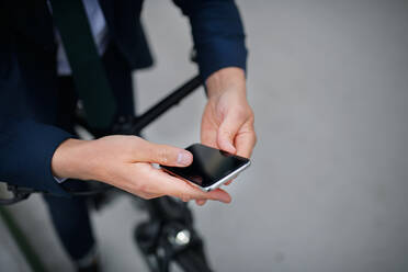 Nahaufnahme eines Geschäftsmannes auf dem Weg zur Arbeit, der sein Fahrrad schiebt und sein Mobiltelefon benutzt, Konzept des nachhaltigen Lebensstils. - HPIF01792