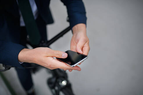 Nahaufnahme eines Geschäftsmannes auf dem Weg zur Arbeit, der sein Fahrrad schiebt und sein Mobiltelefon benutzt, Konzept des nachhaltigen Lebensstils. - HPIF01792