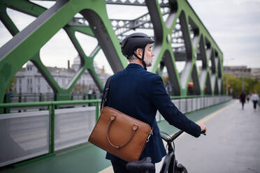 Ein Geschäftsmann auf dem Weg zur Arbeit, der mit dem Fahrrad über eine Brücke fährt, Konzept des nachhaltigen Lebensstils, Rückansicht. - HPIF01793