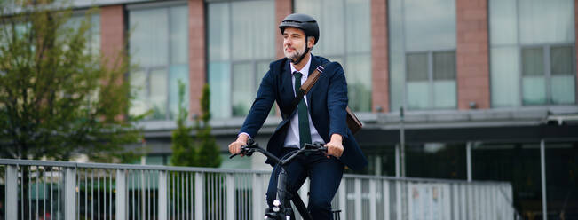 A businessman commuter on the way to work, riding bike in city, sustainable lifestyle concept. Wide photography. - HPIF01794