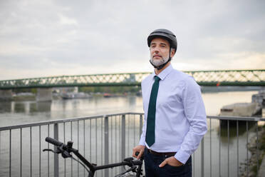Ein Geschäftsmann auf dem Weg zur Arbeit, auf der Brücke stehend und mit dem Fahrrad, Konzept des nachhaltigen Lebensstils. - HPIF01795