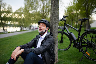 A businessman with bike sitting on grass in park, enjoying leisure time. Commuting and alternative transport concept. - HPIF01797