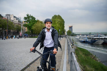 Ein Geschäftsmann auf dem Weg zur Arbeit, der mit dem Fahrrad am Fluss entlang fährt, ein nachhaltiges Lebensstilkonzept. - HPIF01801