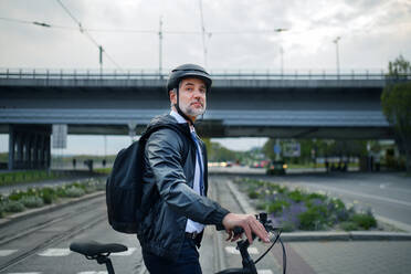Ein Geschäftsmann auf dem Weg zur Arbeit, der die Straße mit dem Fahrrad überquert, Konzept des nachhaltigen Lebensstils. - HPIF01815
