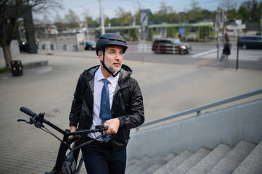 Ein Geschäftsmann auf dem Weg zur Arbeit, der sein Fahrrad nach oben trägt, ein nachhaltiges Lebensstilkonzept. - HPIF01816