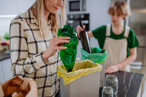 A mother with daughter throwing empty plastic and glass bottles in recycling bin in kitchen. - HPIF01831