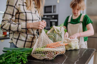 A mother unpacking local food in zero waste packaging from bag with help of daughter in kitchen at home. - HPIF01838