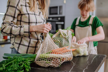 Eine Mutter packt mit Hilfe ihrer Tochter in der heimischen Küche einheimische Lebensmittel in einer abfallfreien Verpackung aus einer Tüte aus. - HPIF01838