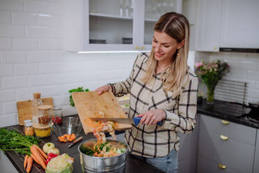 Eine Frau wirft Gemüseschnipsel in einen Kompostkübel in der Küche. - HPIF01845