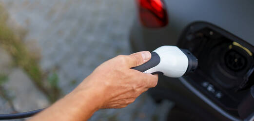 A man holding power supply cable at electric vehicle charging station, closeup - HPIF01859