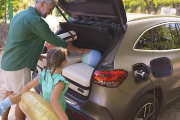 Eine Familie mit kleinen Kindern, die ihr Auto belädt und darauf wartet, dass das Auto aufgeladen wird, bevor sie zum Picknick aufbricht. - HPIF01861