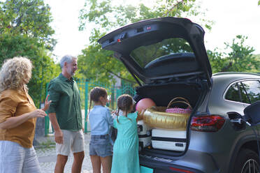 Eine Familie mit kleinen Kindern belädt ihr Auto und wartet darauf, dass es aufgeladen wird, bevor sie in den Urlaub fährt. - HPIF01863