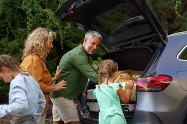 Eine glückliche Familie bereitet sich auf den Urlaub vor, indem sie ihre Koffer in den Kofferraum packt, während ihr Elektroauto aufgeladen wird. - HPIF01870