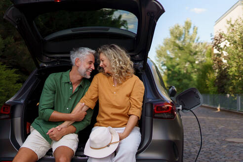 A middle-aged couple sitting in trunk while waiting for charging car before travelling on summer holiday. - HPIF01878