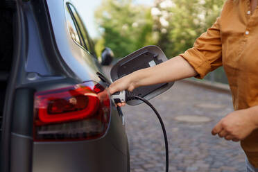 A woman holding power supply cable at electric vehicle charging station, closeup - HPIF01881