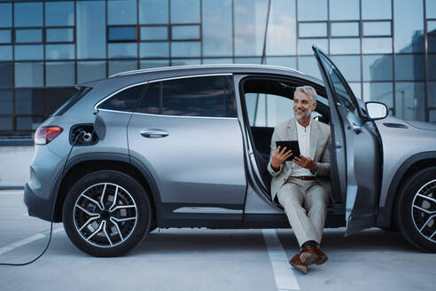 Businessman using tablet while charging a car at electric vehicle charging station, close-up. - HPIF01918