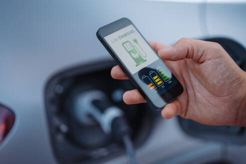 Man setting phone application for charging his electric car at a charging station, closeup. - HPIF01922