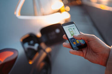 Ein Mann stellt eine Telefonanwendung zum Aufladen seines Elektroautos an einer Ladestation ein, Nahaufnahme. - HPIF01936