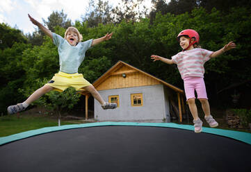 A little siblings enjoy jumping on trampoline - outside in backyard - HPIF01944