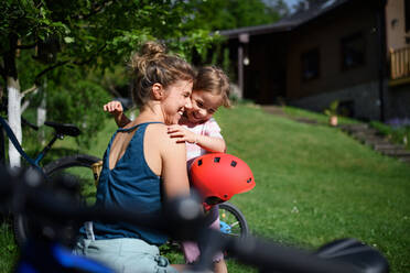 Eine junge Mutter mit ihrer kleinen Tochter bereitet sich auf eine Fahrradtour vor, indem sie die Helme aufsetzen. - HPIF01946