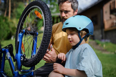 Ein Vater mit seinem kleinen Sohn bereitet das Fahrrad für eine Fahrt vor und pumpt die Reifen im Garten vor dem Haus auf. - HPIF01953