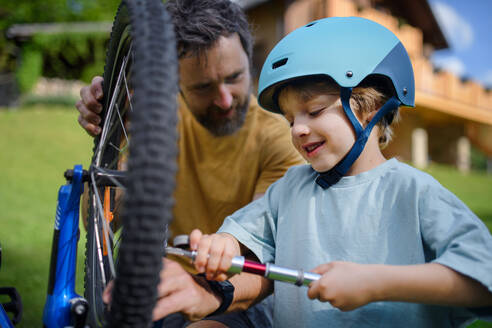 Ein Vater mit seinem kleinen Sohn bereitet das Fahrrad für eine Fahrt vor und pumpt die Reifen im Garten vor dem Haus auf. - HPIF01954