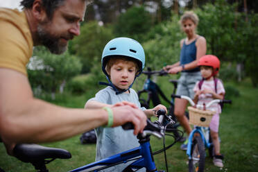 Ein Porträt einer jungen Familie mit kleinen Kindern, die sich auf eine Fahrradtour vorbereiten, stehend mit Fahrrädern in der Natur. - HPIF01963