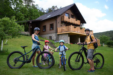 Porträt einer jungen Familie mit kleinen Kindern, die sich auf eine Fahrradtour vorbereiten und mit Fahrrädern vor dem Haus stehen. - HPIF01965