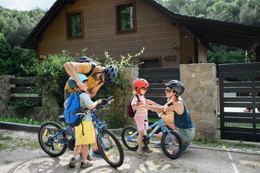 Porträt einer jungen Familie mit kleinen Kindern, die sich auf eine Fahrradtour vorbereiten und mit Fahrrädern vor dem Haus stehen. - HPIF01967