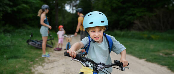 A portrait of excited little boy with his family at backround riding bike on path in park in summer - HPIF01970