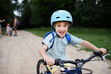 Ein Porträt der aufgeregten kleinen Jungen mit seiner Familie im Hintergrund Radfahren auf dem Weg im Park im Sommer - HPIF01971