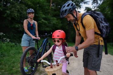 Ein Porträt einer jungen Familie mit kleinen Kindern, die sich auf eine Fahrradtour vorbereiten, stehend mit Fahrrädern in der Natur. - HPIF01972