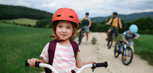 Ein Porträt der aufgeregtes kleines Mädchen mit seiner Familie im Hintergrund Reiten Fahrrad auf Weg im Park im Sommer - HPIF01974