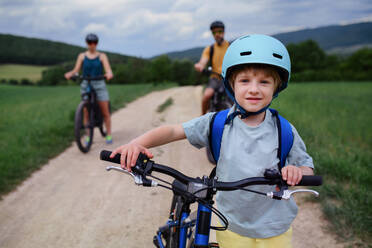 A young family with little child riding bicycles on road in village in summer. - HPIF01975