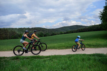 Eine junge Familie mit kleinem Kind fährt im Sommer mit dem Fahrrad auf der Straße in einem Dorf. - HPIF01977