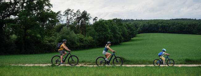 Eine junge Familie mit kleinem Kind fährt im Sommer mit dem Fahrrad auf einem Weg im Park. - HPIF01978