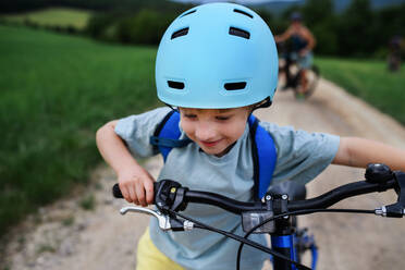 Eine junge Familie mit kleinem Kind fährt im Sommer mit dem Fahrrad auf der Straße in einem Dorf. - HPIF01980