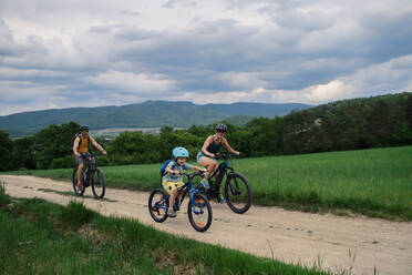 Eine junge Familie mit kleinem Kind fährt im Sommer mit dem Fahrrad auf der Straße in einem Dorf. - HPIF01981