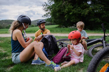 Eine junge Familie mit kleinen Kindern ruht sich nach einer Radtour im Sommer im Gras eines Parks aus. - HPIF01982