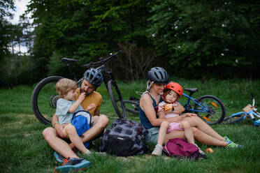 Eine junge Familie mit kleinen Kindern ruht sich nach einer Radtour im Sommer im Gras eines Parks aus. - HPIF01984