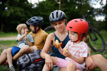 A young family with little children resting after bike ride, sitting on grass in park in summer. - HPIF01985