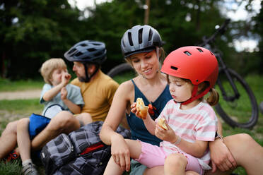 Eine junge Familie mit kleinen Kindern ruht sich nach einer Radtour im Sommer im Gras eines Parks aus. - HPIF01985